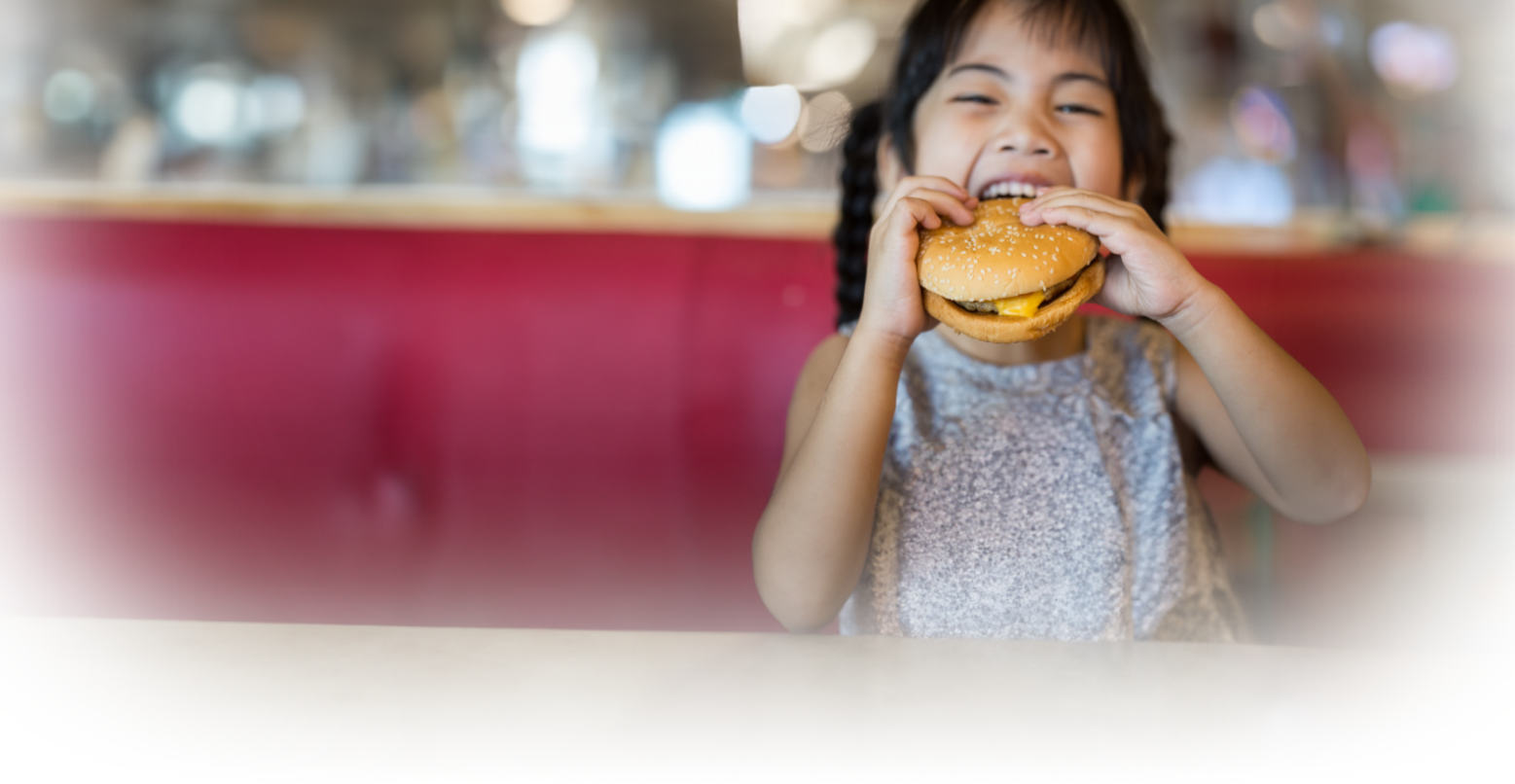 Image of a girl eating a cheeseburger at a diner table