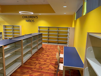 Bright yellow walls, book shelving, a table with chairs, and an orange rug.