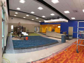 The interior of the main area of new Empire Library. Includes blue and orange carpet being put down, blue and orange walls, lights overhead, and the circulation desk.