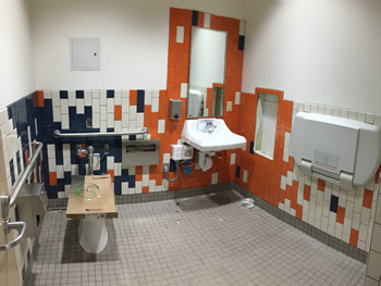 One of the restrooms in the new Empire Library. Includes orange, dark blue, and white tiles with white walls, sink, toilet, and baby changing table.