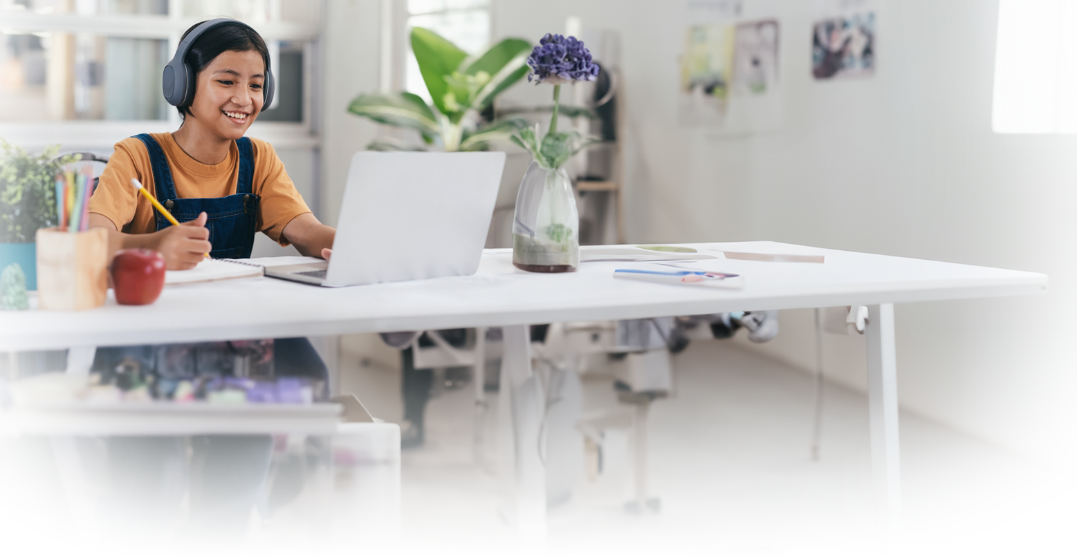 Online Tutoring. The image shows a child sitting at a computer with headphones on and writing on a tablet as if they were in an online tutoring session.