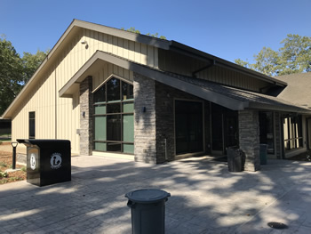 The exterior of the library entrance. The walk area is brick pavers the area around the entrance is stone like bricks. The exterior walls above and to the sides are tan wood siding.